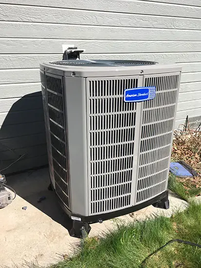 A newly set American Standard outdoor condenser on a pad beside a house
